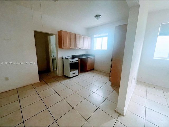 kitchen featuring light brown cabinetry, light tile patterned flooring, and white stove