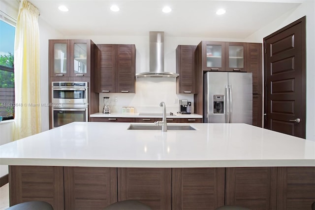 kitchen featuring stainless steel appliances, a large island with sink, wall chimney range hood, and sink