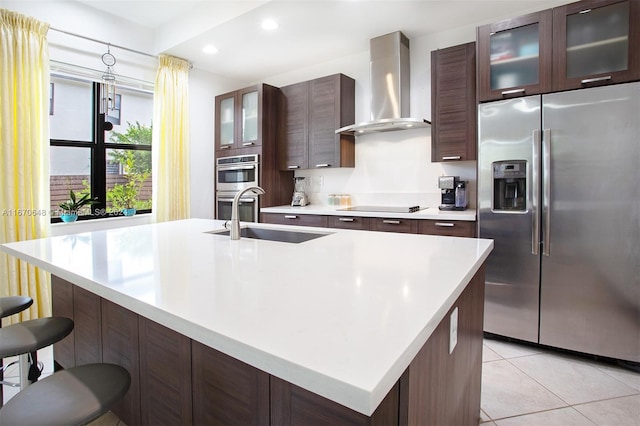 kitchen with light tile patterned floors, a center island with sink, wall chimney exhaust hood, stainless steel appliances, and a kitchen bar