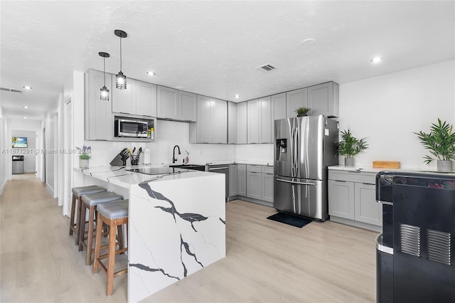 kitchen with decorative light fixtures, gray cabinets, stainless steel appliances, and light hardwood / wood-style flooring