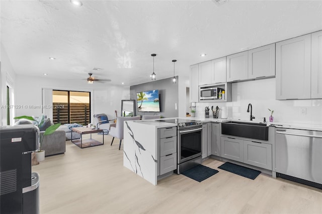 kitchen featuring sink, kitchen peninsula, light hardwood / wood-style flooring, appliances with stainless steel finishes, and decorative light fixtures