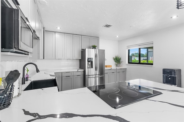 kitchen with sink, gray cabinetry, a textured ceiling, appliances with stainless steel finishes, and light stone countertops