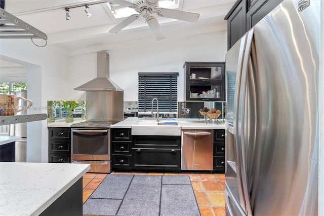 kitchen featuring appliances with stainless steel finishes, lofted ceiling with beams, wall chimney exhaust hood, ceiling fan, and sink