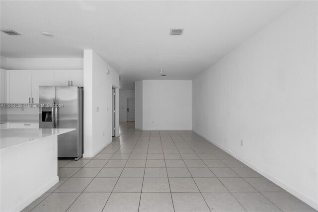 kitchen with stainless steel fridge, light tile patterned flooring, and white cabinets