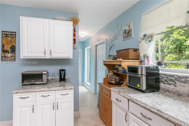 kitchen featuring white cabinets, light tile patterned flooring, light stone countertops, and tasteful backsplash