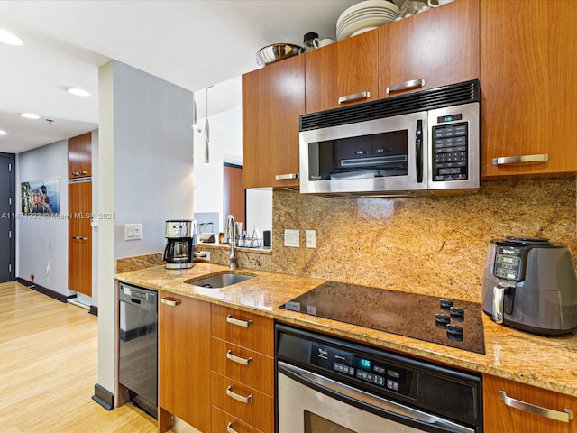 kitchen featuring black appliances, tasteful backsplash, light stone counters, sink, and light hardwood / wood-style floors