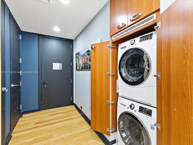 laundry area with cabinets, stacked washing maching and dryer, and light wood-type flooring