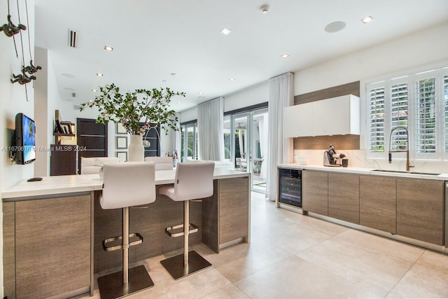 kitchen with wine cooler, a kitchen bar, white cabinetry, and a wealth of natural light