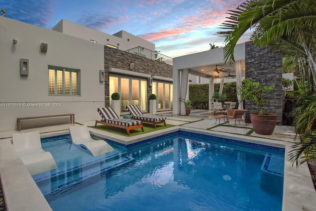 pool at dusk with ceiling fan and a patio