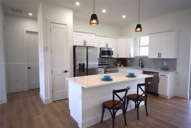 kitchen with white cabinets, a center island, hardwood / wood-style floors, and appliances with stainless steel finishes