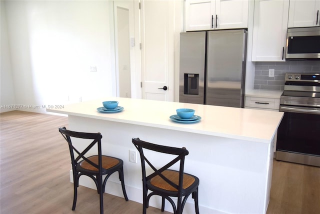 kitchen featuring appliances with stainless steel finishes, backsplash, a kitchen breakfast bar, white cabinets, and a kitchen island