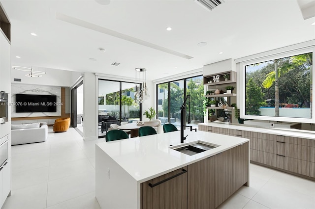 kitchen with light tile patterned floors, a center island with sink, decorative light fixtures, and sink