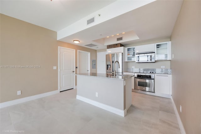 kitchen with appliances with stainless steel finishes, white cabinetry, light stone counters, a kitchen island, and sink