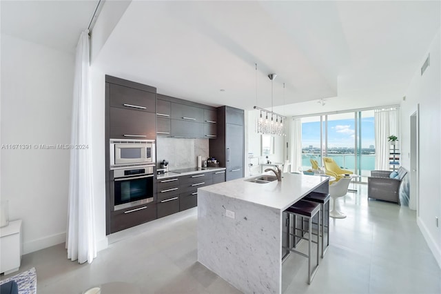 kitchen with sink, hanging light fixtures, stainless steel appliances, a water view, and a center island with sink