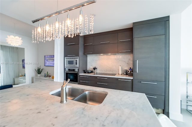 kitchen featuring appliances with stainless steel finishes, decorative backsplash, light stone counters, pendant lighting, and sink