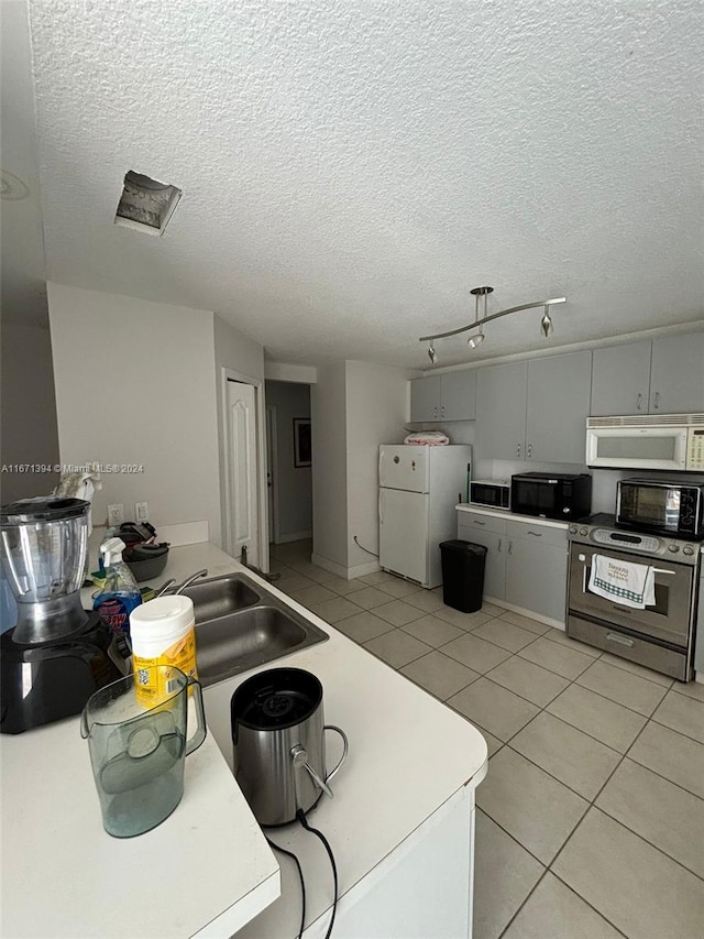 kitchen with a textured ceiling, white appliances, light tile patterned floors, and gray cabinets