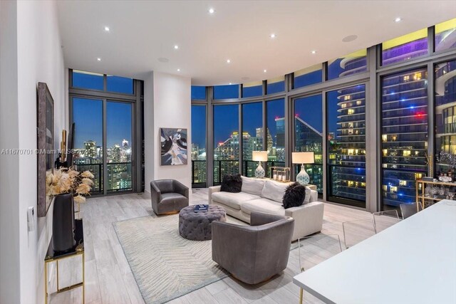 living room with light wood-type flooring, floor to ceiling windows, a high ceiling, and a healthy amount of sunlight