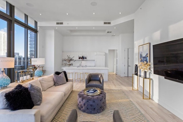 living room featuring light hardwood / wood-style flooring, a towering ceiling, a raised ceiling, and floor to ceiling windows