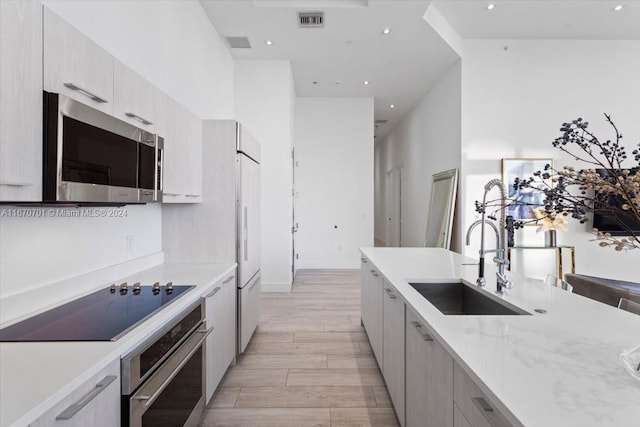 kitchen with light stone countertops, stainless steel appliances, a high ceiling, light hardwood / wood-style flooring, and sink