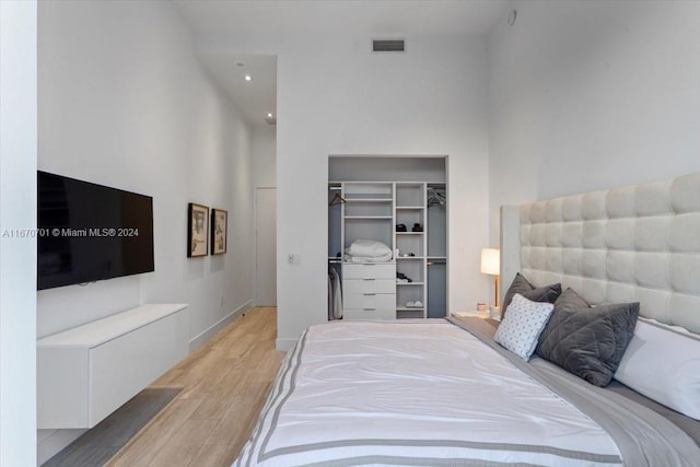 bedroom with light wood-type flooring, a towering ceiling, and a closet