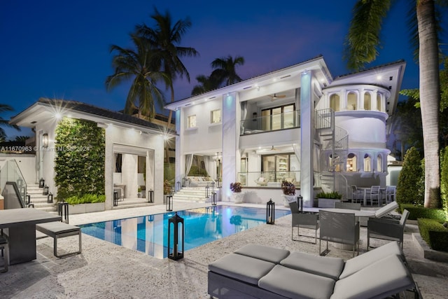 back of house at twilight featuring outdoor dining area, a patio area, ceiling fan, stairs, and an outdoor pool