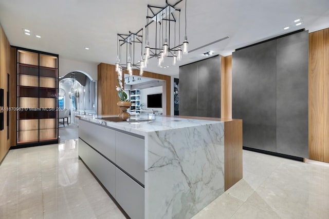 kitchen featuring a spacious island, light stone countertops, black electric stovetop, pendant lighting, and a notable chandelier