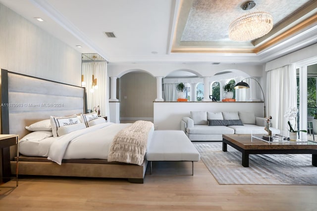 bedroom featuring crown molding, a tray ceiling, light hardwood / wood-style flooring, and a chandelier