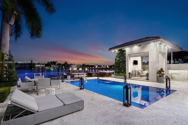 pool at dusk with an outdoor structure, a patio area, and a fenced in pool