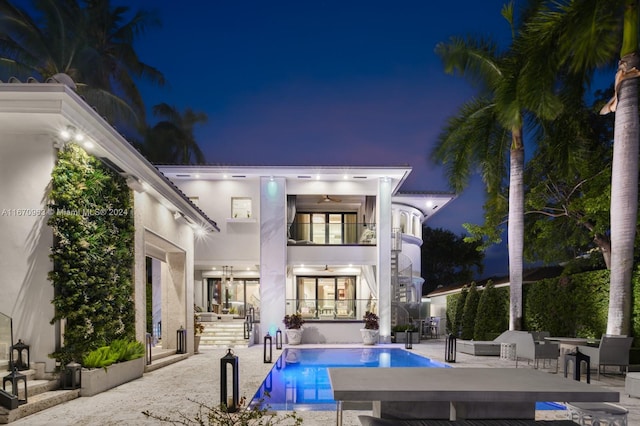 back of house at twilight with stucco siding, a fenced in pool, a patio, a balcony, and a ceiling fan