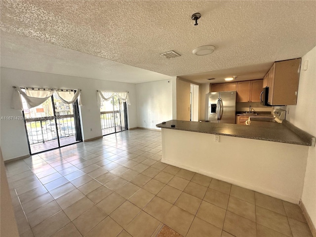 kitchen featuring range, stainless steel fridge, a textured ceiling, light tile patterned flooring, and kitchen peninsula