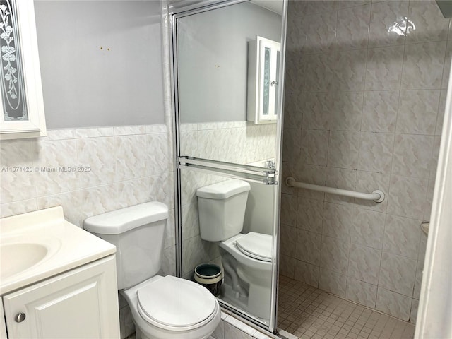 bathroom with a tile shower, vanity, tile walls, and toilet