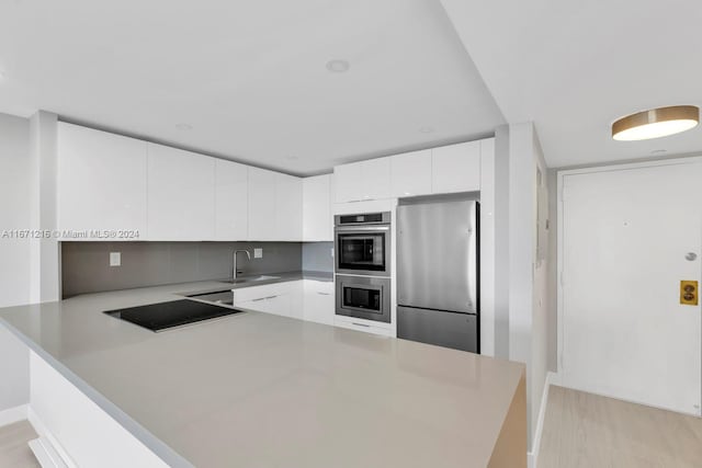 kitchen featuring kitchen peninsula, sink, white cabinetry, light wood-type flooring, and appliances with stainless steel finishes