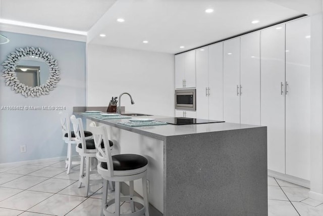 kitchen with white cabinets, light tile patterned floors, sink, stainless steel microwave, and a kitchen bar