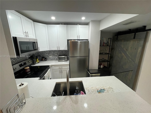 kitchen with white cabinets, sink, a barn door, appliances with stainless steel finishes, and backsplash