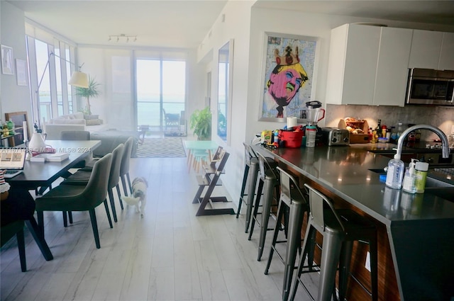 kitchen with white cabinets, sink, light hardwood / wood-style flooring, backsplash, and a kitchen bar