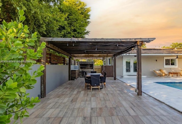 patio terrace at dusk featuring a fenced in pool, french doors, and an outdoor kitchen