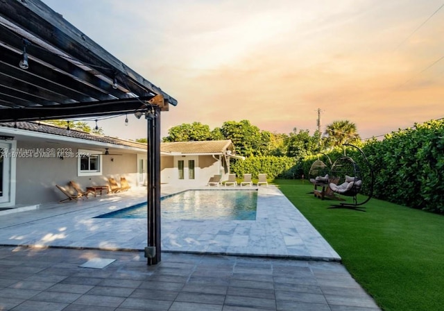 pool at dusk featuring a lawn and a patio