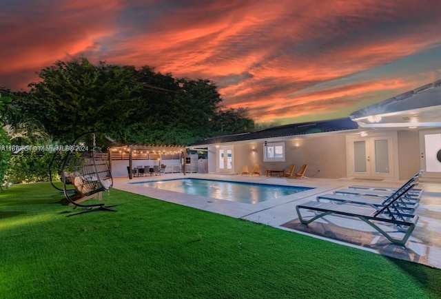 pool at dusk with a lawn, a patio, and french doors