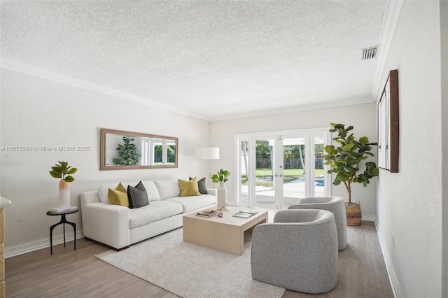 living room featuring ornamental molding, light wood-type flooring, french doors, and a textured ceiling