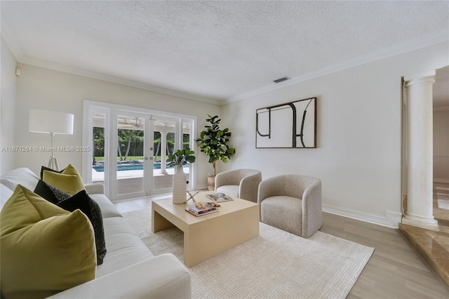 living room featuring light wood finished floors, french doors, a textured ceiling, crown molding, and ornate columns