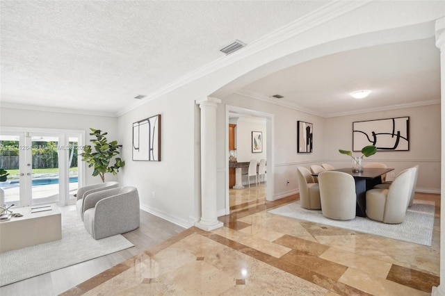 living room featuring baseboards, visible vents, arched walkways, a textured ceiling, and ornate columns