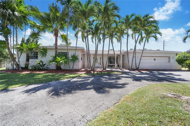 single story home featuring driveway, a garage, concrete block siding, and a front yard