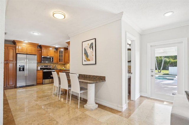 kitchen featuring a kitchen bar, ornamental molding, stainless steel appliances, and tasteful backsplash