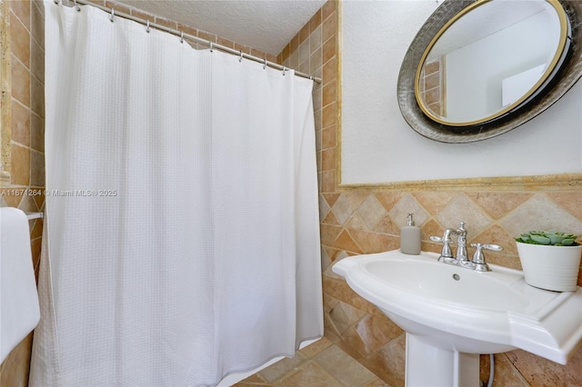 full bath featuring a textured ceiling, a sink, tile walls, and tile patterned floors