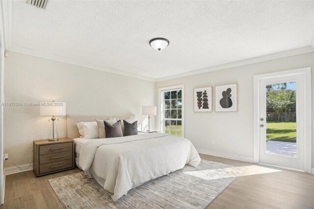 bedroom with a textured ceiling, light hardwood / wood-style floors, access to exterior, and ornamental molding