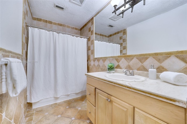 full bathroom featuring visible vents, shower / bathtub combination with curtain, a textured ceiling, vanity, and tile walls