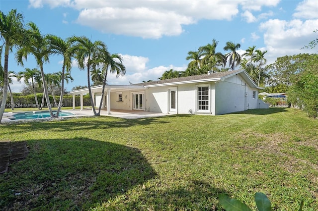 back of property featuring stucco siding, an outdoor pool, a lawn, and a patio