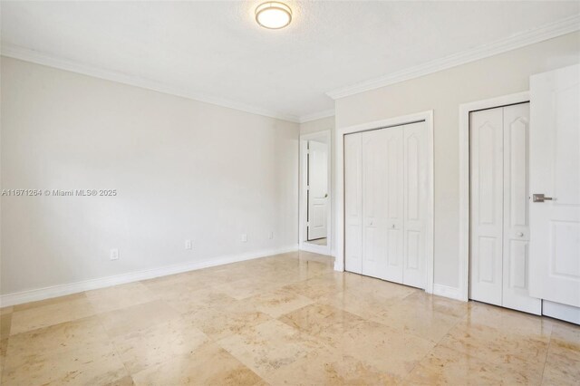 unfurnished bedroom with ornamental molding, a textured ceiling, and two closets