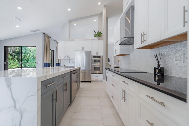 kitchen with appliances with stainless steel finishes, dark stone counters, wall chimney range hood, and white cabinets