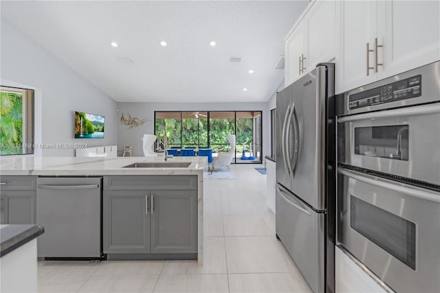 kitchen with appliances with stainless steel finishes, gray cabinetry, vaulted ceiling, and white cabinets